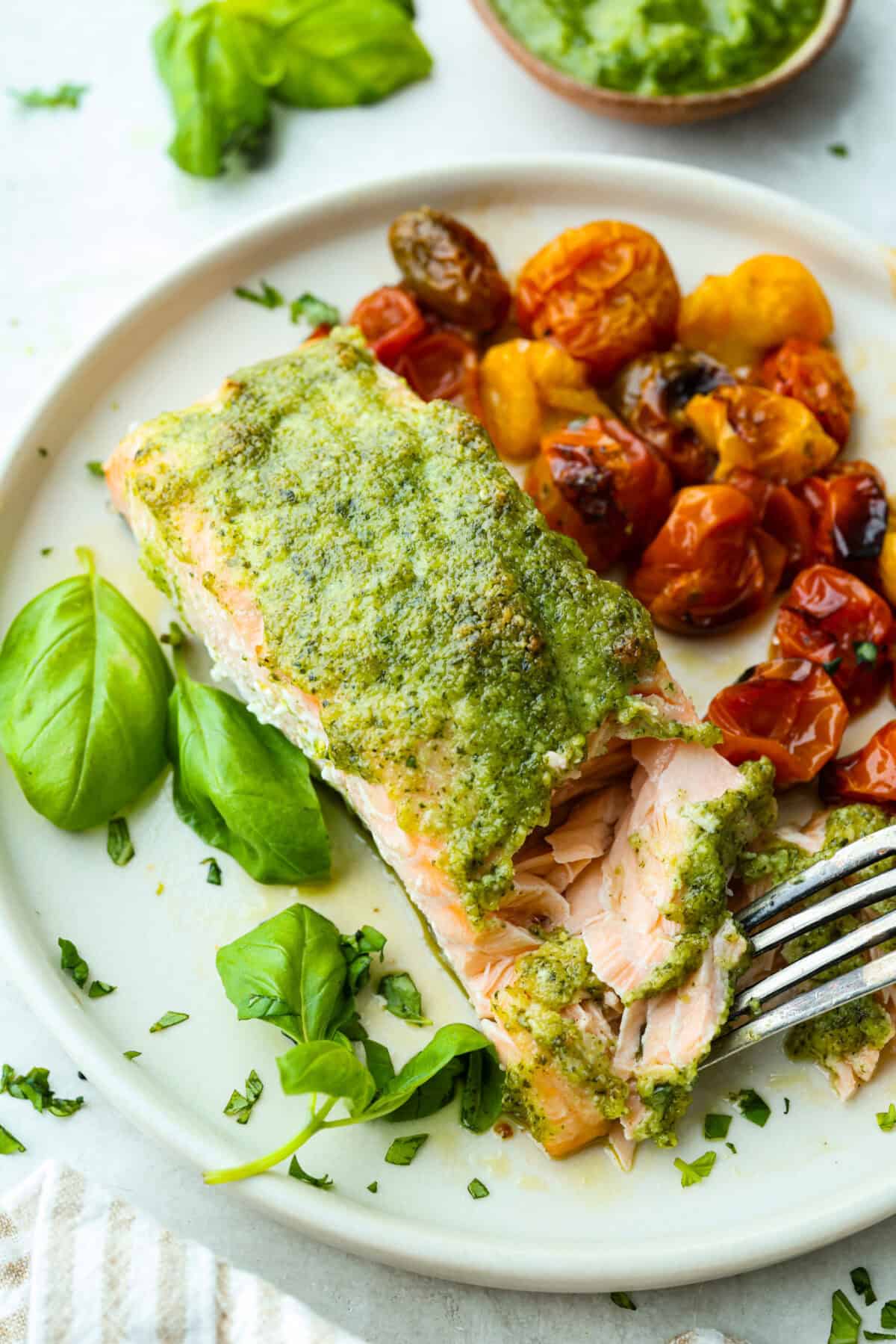 Plated pesto salmon fillet with cooked cherry tomatoes next to it. 