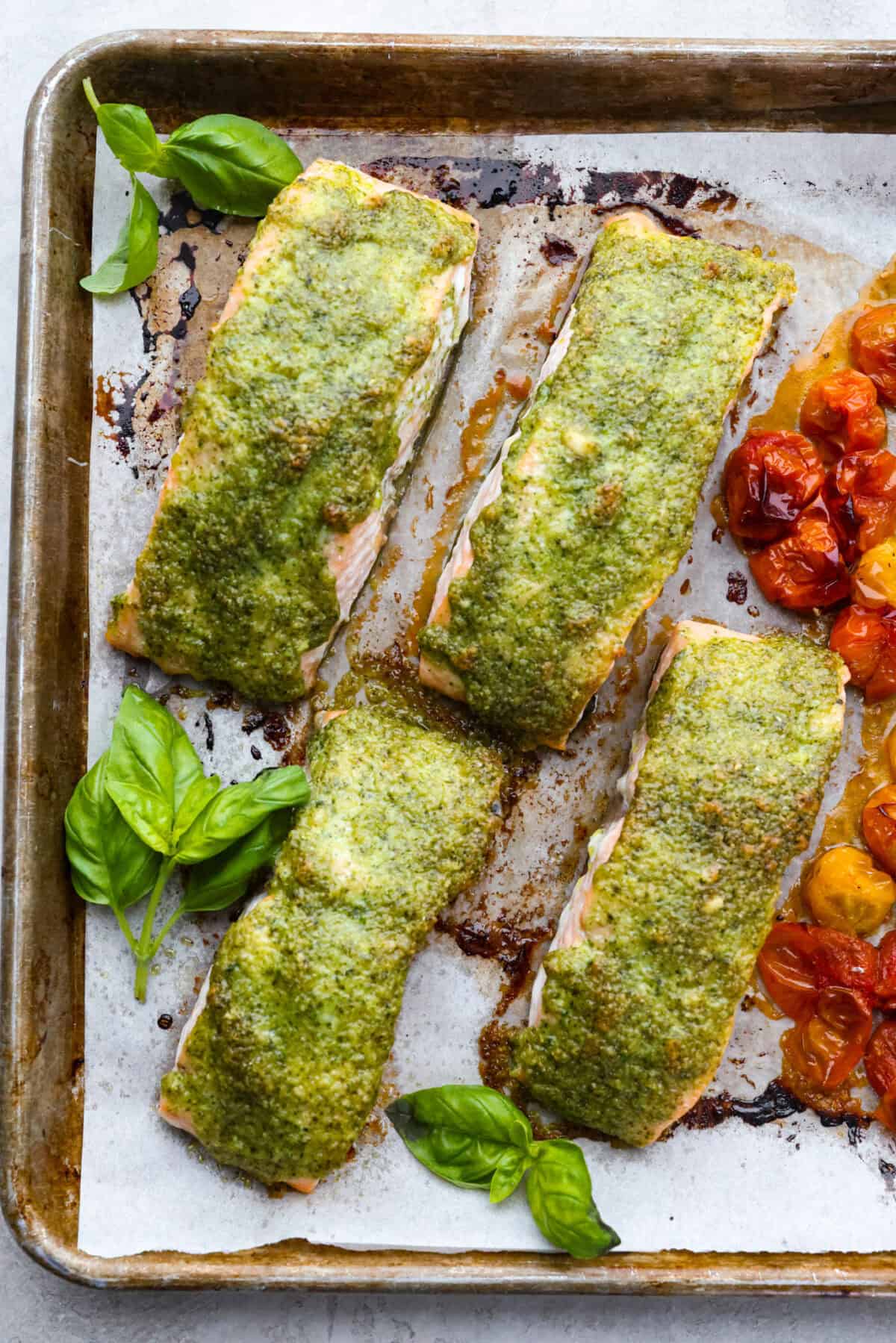 Pesto Salmon is everything. Itโs one of the easiest, lightest, most flavor-packed dinners Iโve ever made! It uses just 6 ingredients, takes 30 minutes, and it looks like you totally have your life together (even if you donโt;). Cooked pesto salmon next to cooked cherry tomatoes on a baking sheet.