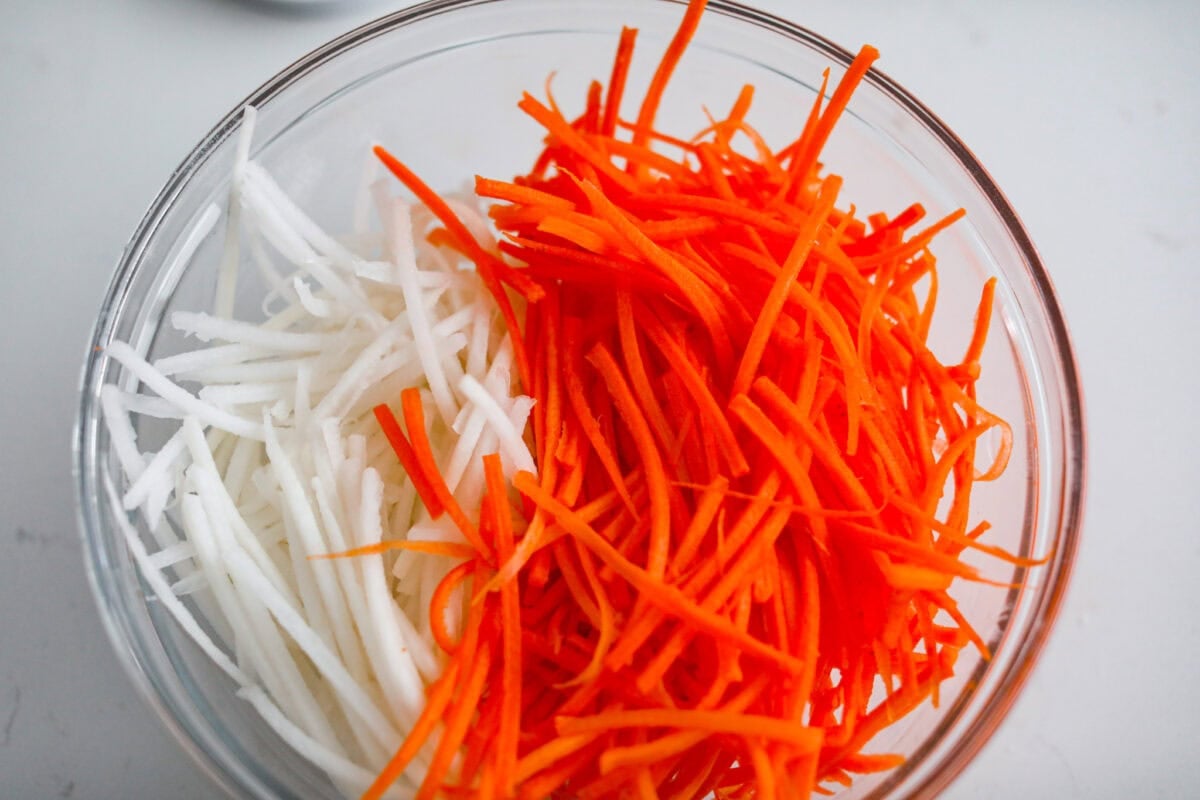 My pickled carrots and daikon are the zesty upgrade your meals didn’t know they needed! Made with rice vinegar, they’re a little sweeter and less sharp than typical pickled veggies. Julienned carrots and radishes in a bowl.