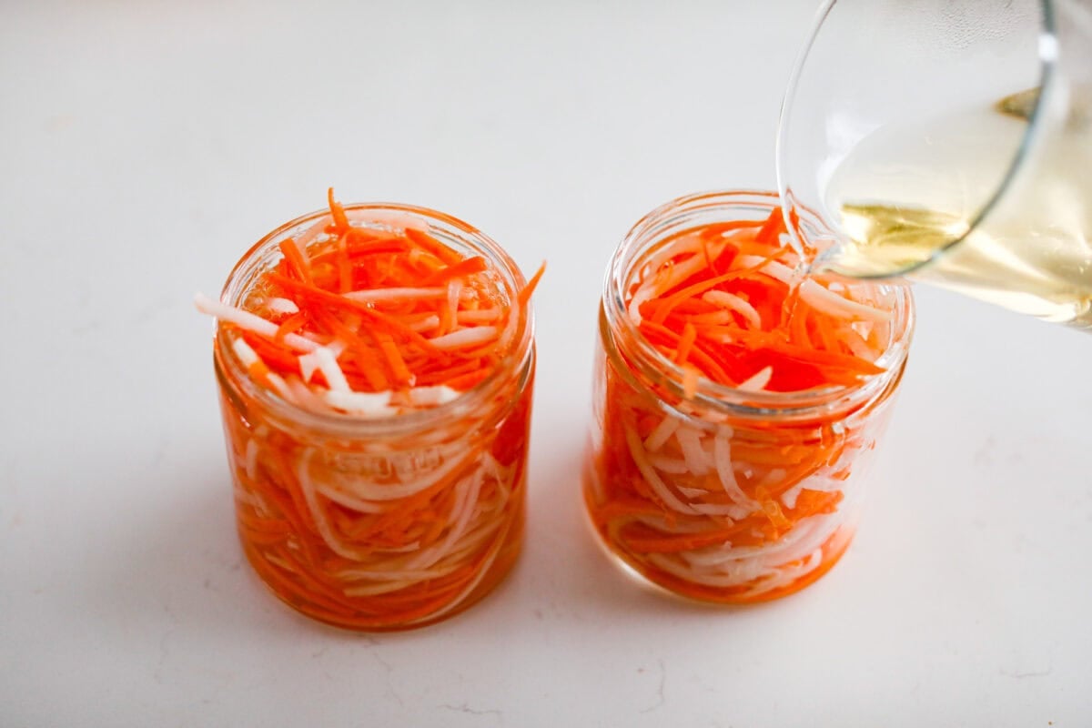 My pickled carrots and daikon are the zesty upgrade your meals didn’t know they needed! Made with rice vinegar, they’re a little sweeter and less sharp than typical pickled veggies. Someone pouring brine into two mason jars filled with julienned daikon and carrots.