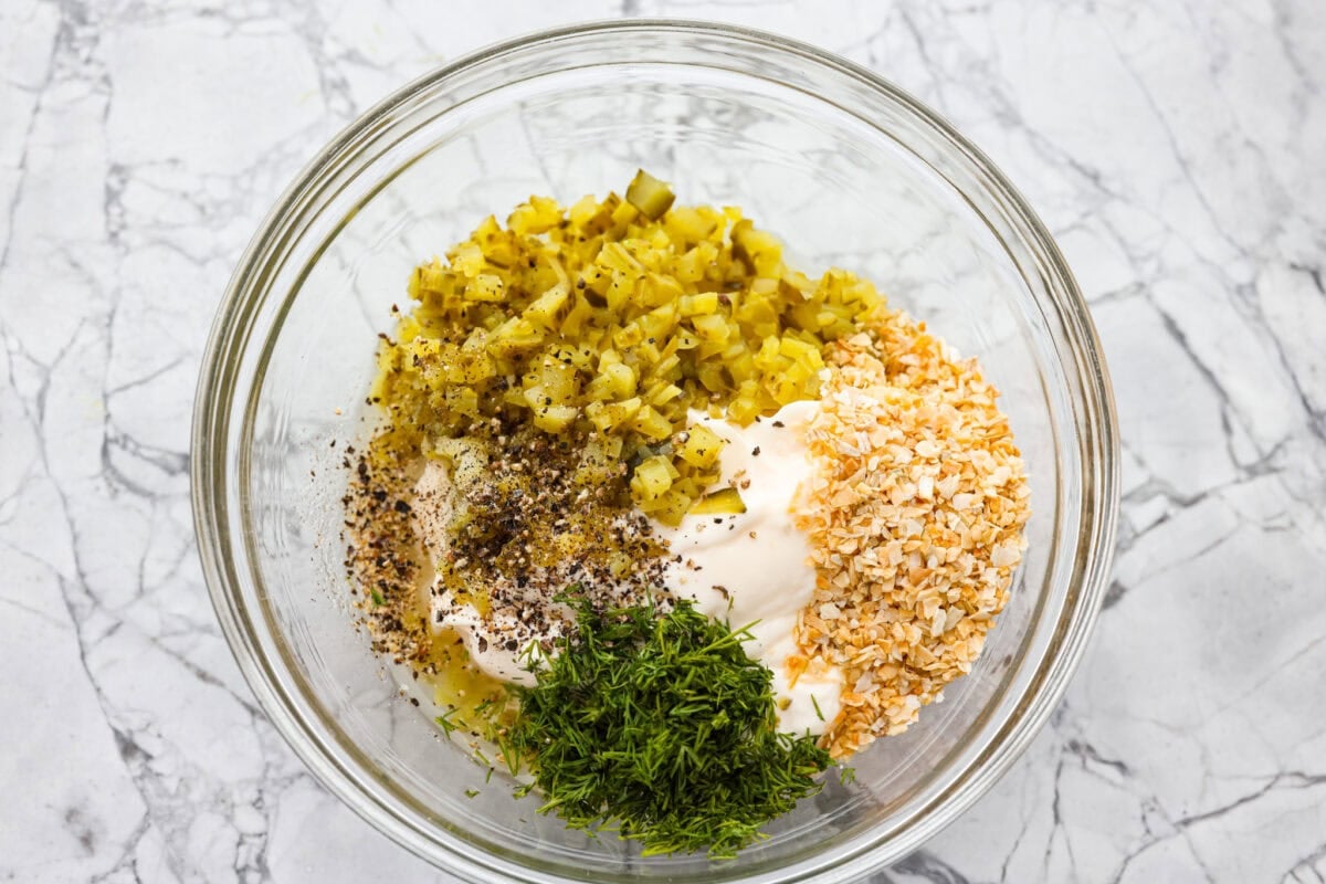 Tartar Sauce uses fresh herbs and my favorite, crunchy dill pickles. My recipe is unique because it uses dried onion, giving it the best punch of flavor and texture! All of the ingredients added to a bowl.