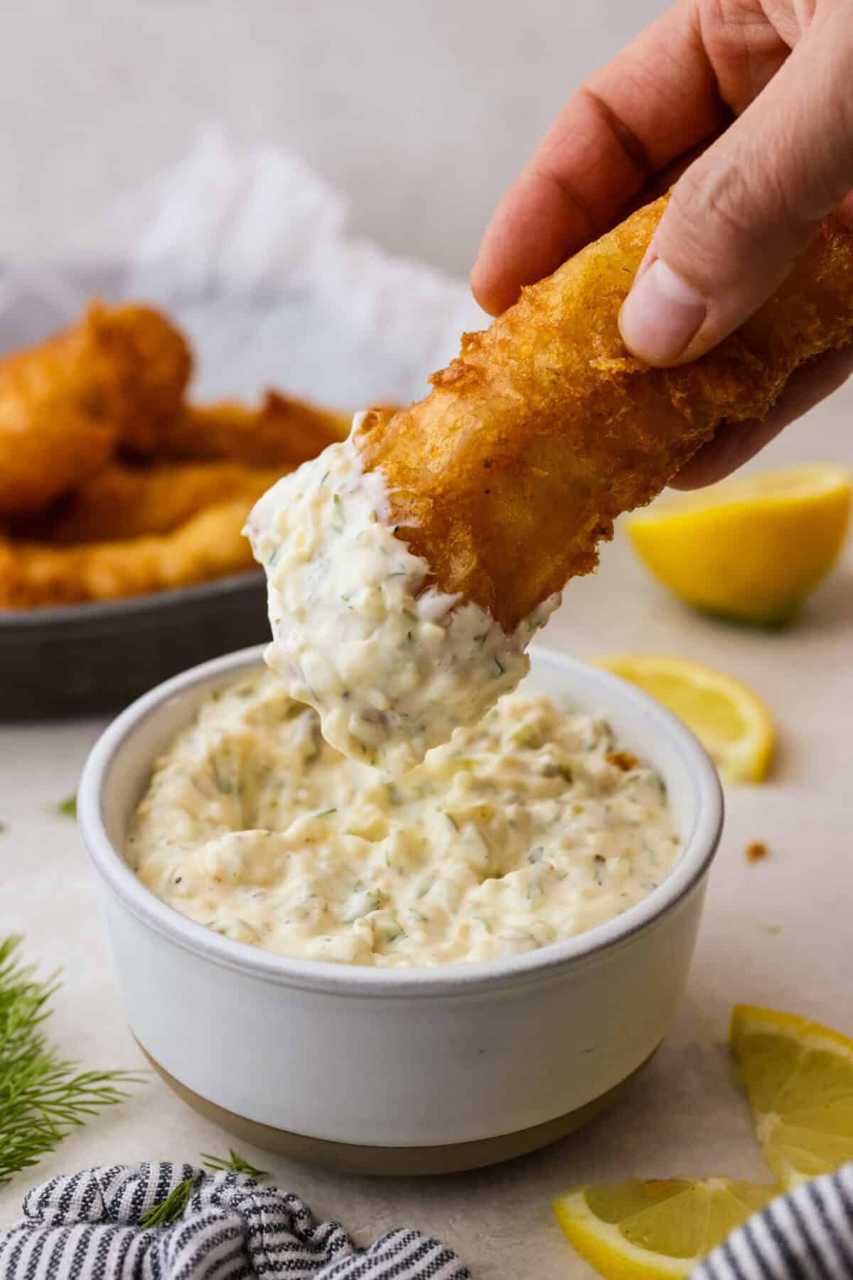 Tartar Sauce uses fresh herbs and my favorite, crunchy dill pickles. My recipe is unique because it uses dried onion, giving it the best punch of flavor and texture! Someone dipping a fish stick into a bowl of tartar sauce.