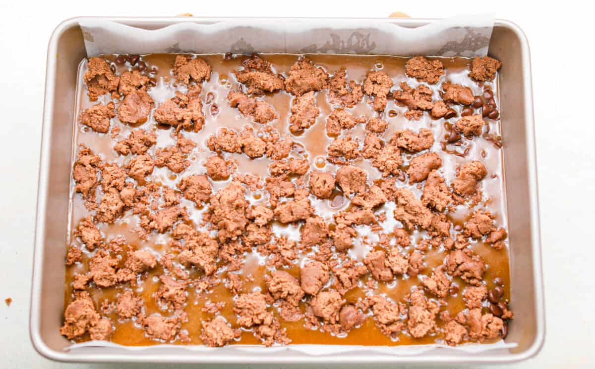Caramel brownies just got easier! Made with cake mix and melted caramel candies, they’re rich, gooey, egg-free, and fuss-free. This will be your new favorite shortcut dessert! Pieces of brownie batter crumbled over the top of the caramel ready to go into the oven.