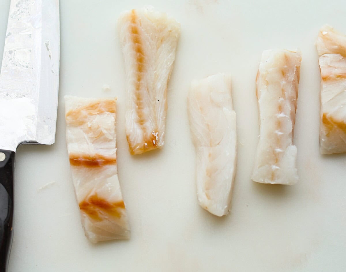Skip the overpriced takeout and bring the pub vibes home! Crispy, golden fish and chips—light, flaky, pan-fried perfection. It’s cheaper, easier, and honestly? Way better than anything stuffed in a greasy paper bag. Fish fillets cut and drying on a cutting board.