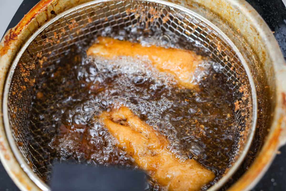 Skip the overpriced takeout and bring the pub vibes home! Crispy, golden fish and chips—light, flaky, pan-fried perfection. It’s cheaper, easier, and honestly? Way better than anything stuffed in a greasy paper bag. Fish fillets frying in oil in a frying basket.