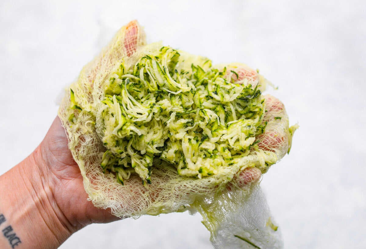 You better believe I count down to zucchini season so I know when I can make this delicious Zucchini Bread! It’s moist, perfectly spiced, and loaded with the best flavor and a hint of veggies! Someone using cheesecloth to squeeze out the excess liquid from the shredded zucchini.