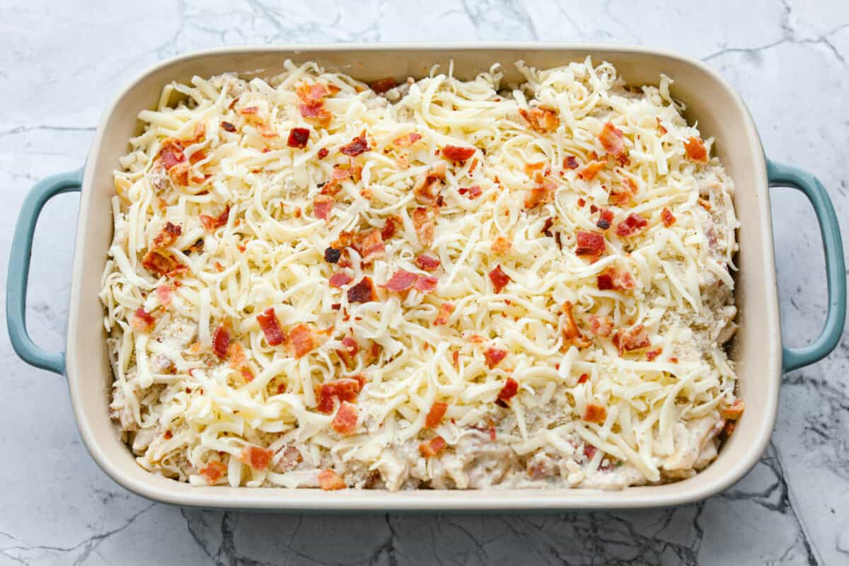 Want to make something you know your kids will eat? This chicken bacon ranch casserole is it! I can't tell you how delicious this casserole is! The combination of flavors is perfection! You have to try it! Casserole ingredients in a baking dish with cheese and bacon on top.