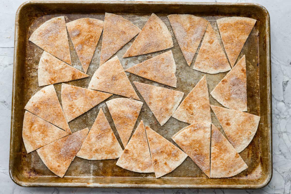You have to try these cinnamon sugar tortilla chips! They're sweet, crispy, and totally addictive. They’re perfect for scooping up your favorite dessert dips or gobbling them down on their own! Triangles spread out on a cookie sheet ready to go into the oven.
