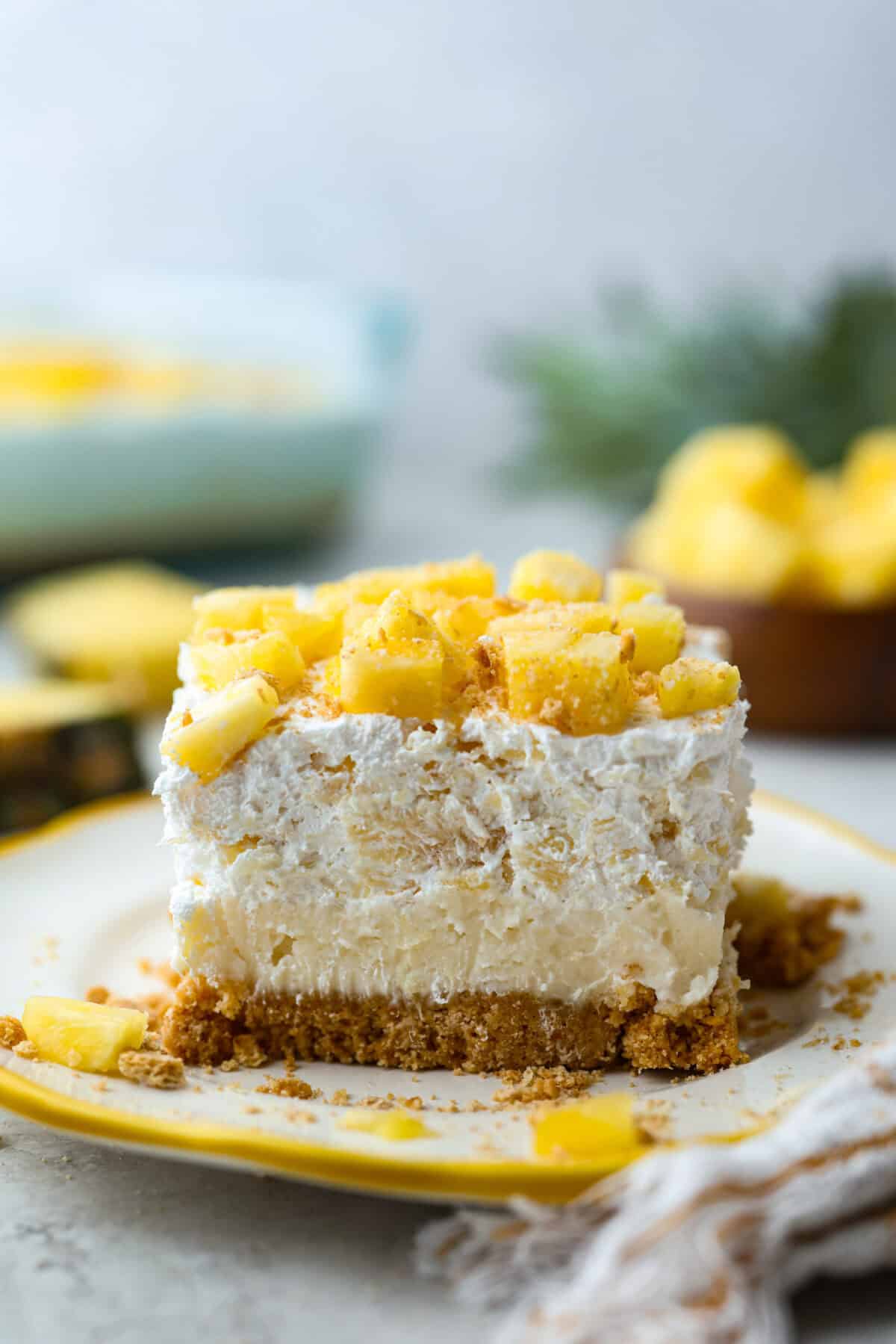 Craving a bright and sunny dessert? This pineapple delight will hit the spot! With a buttery crust, creamy filling, and sweet pineapple topping, it’s light, tropical, and totally irresistible! Side shot of a slice of pineapple delight layered dessert.