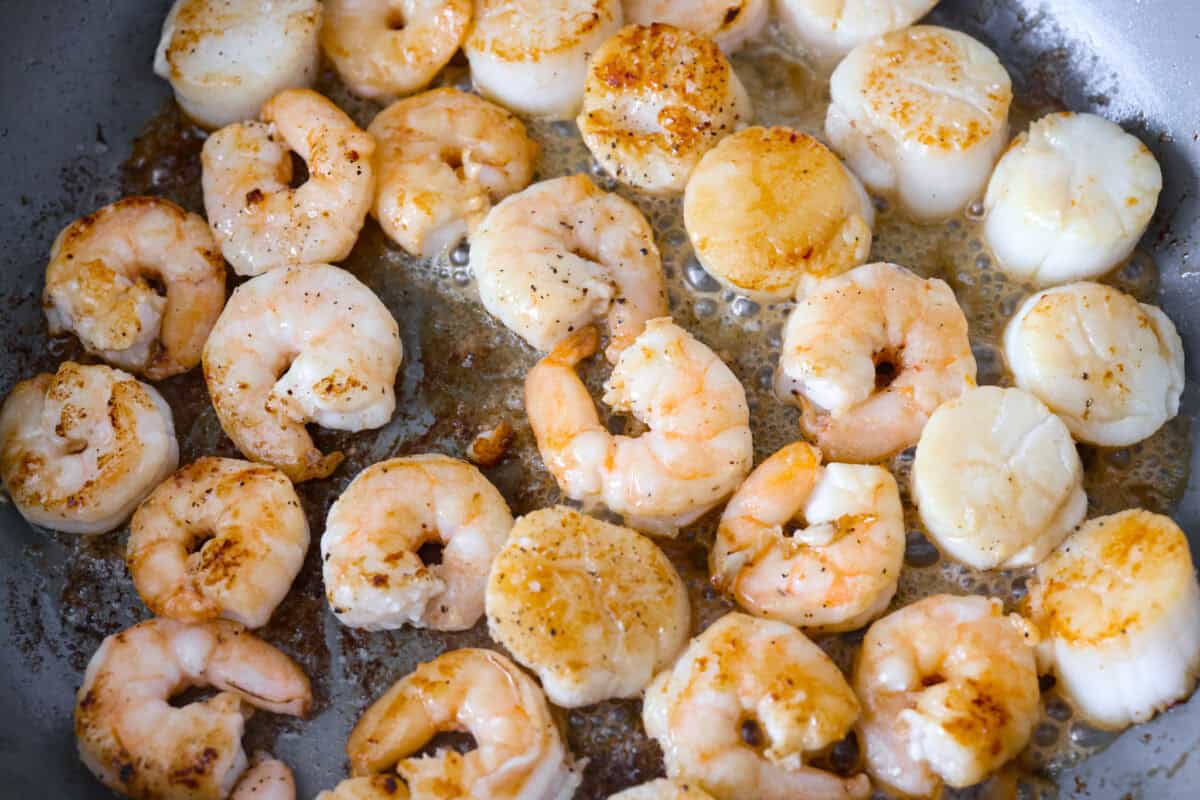 My seafood pasta has a silky lemon garlic cream sauce that is to die for! It's loaded with tender shrimp, scallops, and mussels. Itโs the perfect date night dish! Shrimp and scallops cooking in butter.