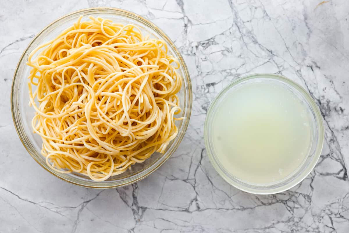 My seafood pasta has a silky lemon garlic cream sauce that is to die for! It's loaded with tender shrimp, scallops, and mussels. Itโs the perfect date night dish! Cooked pasta in a bowl next to a bowl of reserved pasta water.