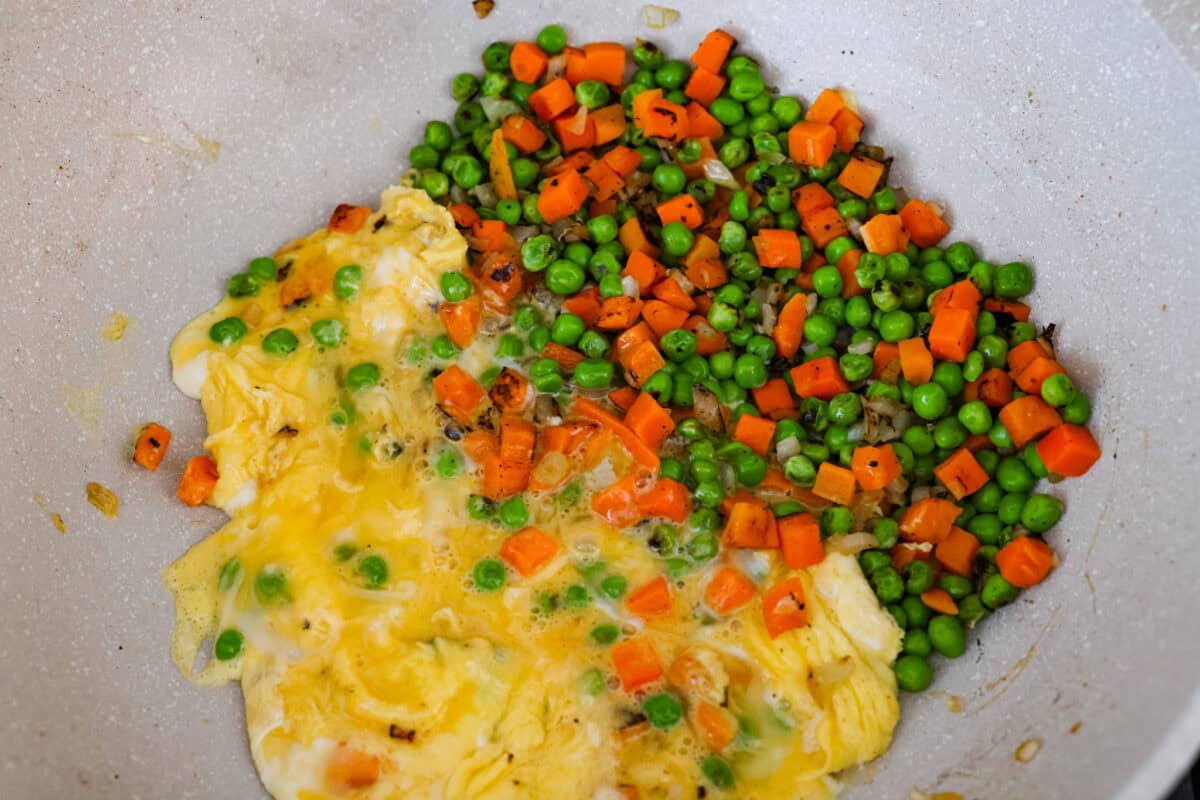 Skip the takeout! This shrimp fried rice is faster, fresher, and way more flavorful! Juicy shrimp, tender veggies, fluffy rice, and scrambled eggs all come together in one irresistible skillet meal. Eggs being cooked next to the veggies in a skillet.