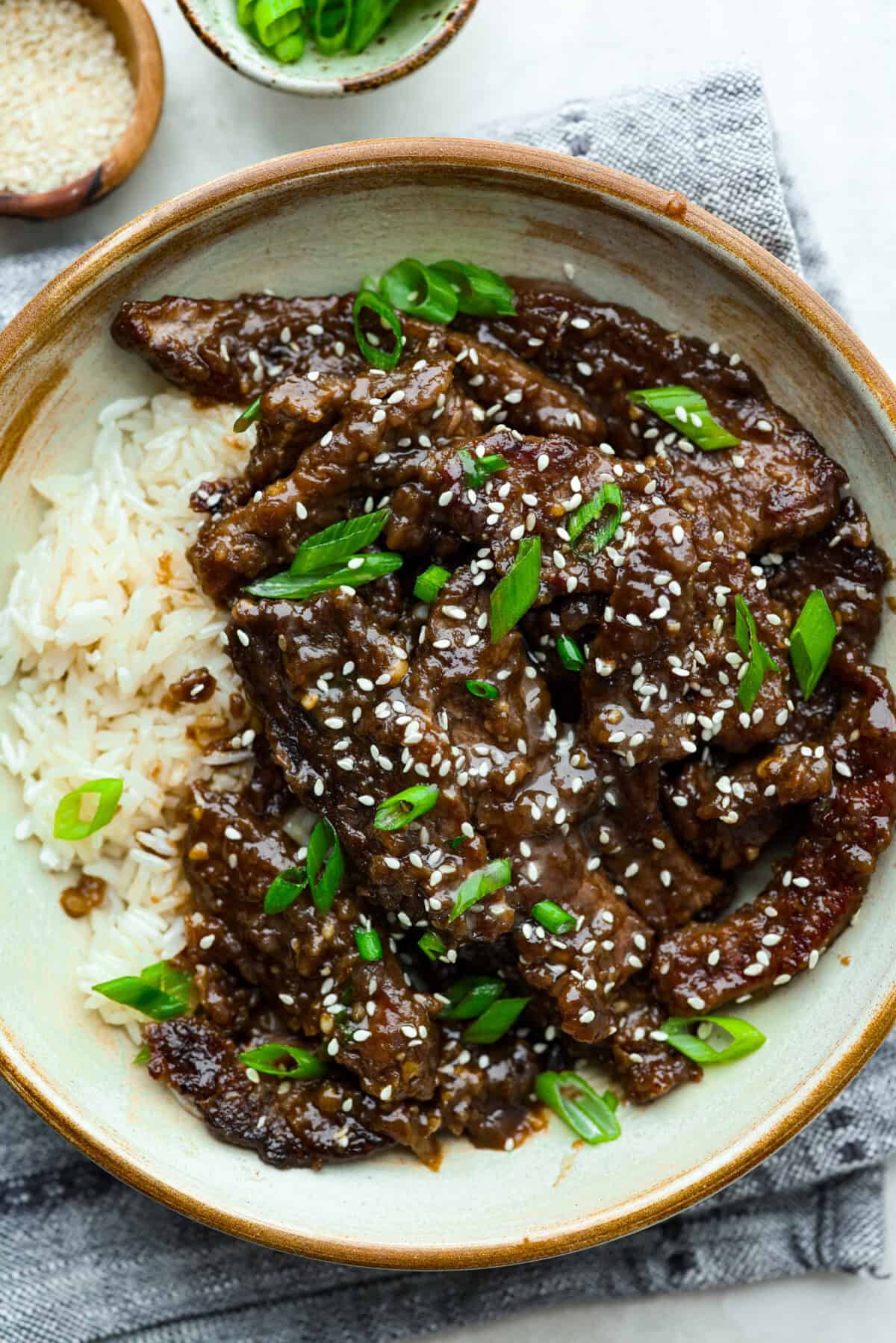 My family is obsessed with my better-than-takeout Beef Teriyaki. The secret? Velveting the beef! It’s simple, but it makes it unbelievably tender. Trust me, you’ll want this trick in your back pocket. Bowl of garnished beef teriyaki with white rice, sesame seeds and green onions.
