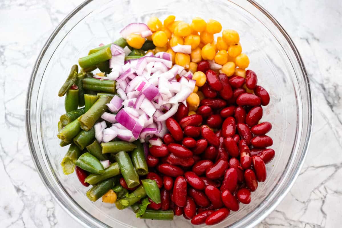Iโve been adding fiber into my meals, and this three bean salad makes it way too easy. Itโs packed with fiber, and still tastes like a treat! It's tangy, a little sweet, and even better the next day. Overhead shot of different beans and onions in a bowl.