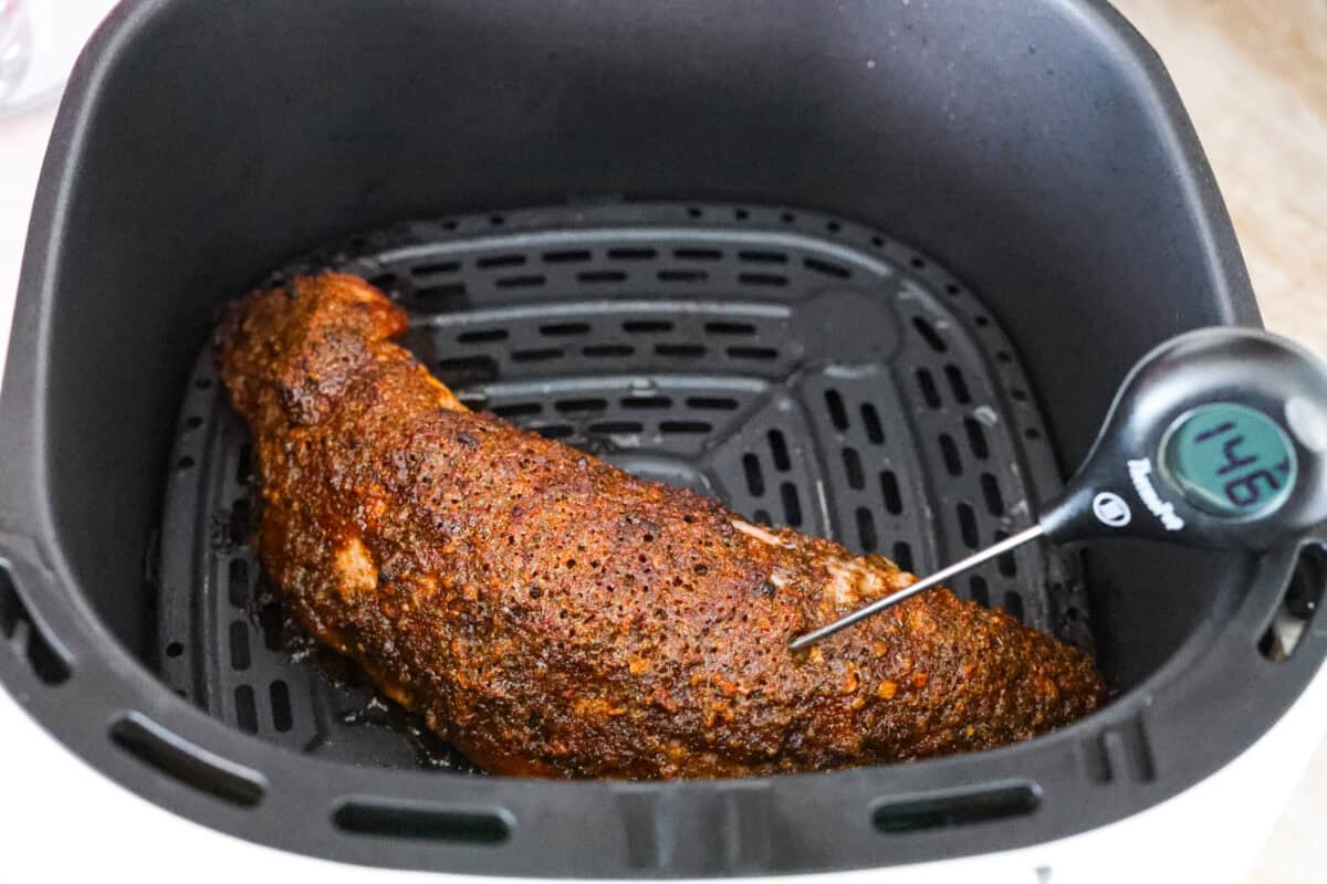 Air fryer pork tenderloin is the ultimate weeknight dinner hero! It's quick, juicy, and packed with flavor! It cooks up perfectly with minimal effort, thanks to a simple marinade and the magic of the air fryer. Someone checking the internal temperature of the meat with a thermometer.