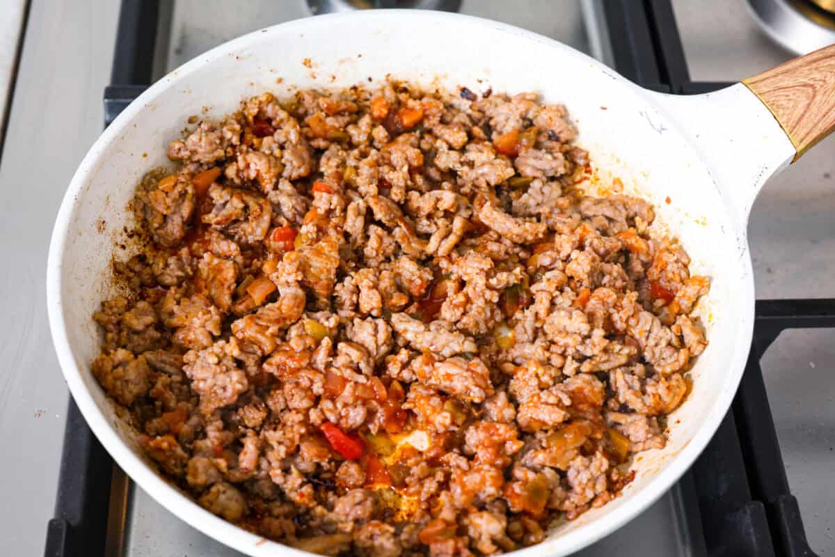 My easy breakfast enchiladas are packed with sausage, fluffy eggs, and zesty salsa, then smothered in a rich, creamy sauce that puts every other breakfast to shame. You can even make them ahead! Sausage cooking an a skillet with salsa added to it.