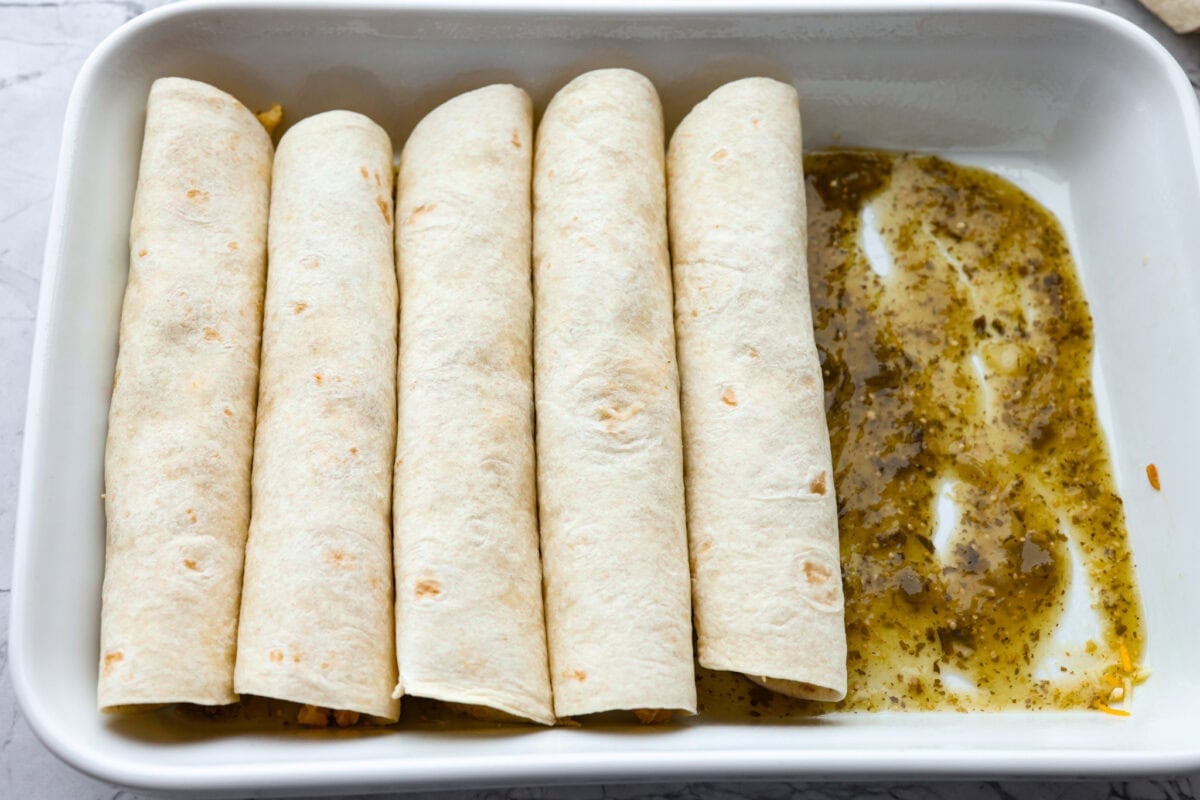 My easy breakfast enchiladas are packed with sausage, fluffy eggs, and zesty salsa, then smothered in a rich, creamy sauce that puts every other breakfast to shame. You can even make them ahead! Rolled enchiladas in a pan with salsa verde on the bottom.