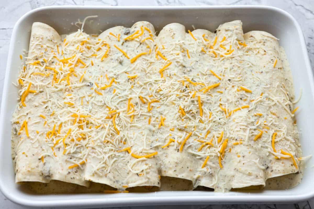 My easy breakfast enchiladas are packed with sausage, fluffy eggs, and zesty salsa, then smothered in a rich, creamy sauce that puts every other breakfast to shame. You can even make them ahead! All of the breakfast enchiladas rolled up in the pan with creamy enchilada sauce on top and cheese sprinkled on as well.