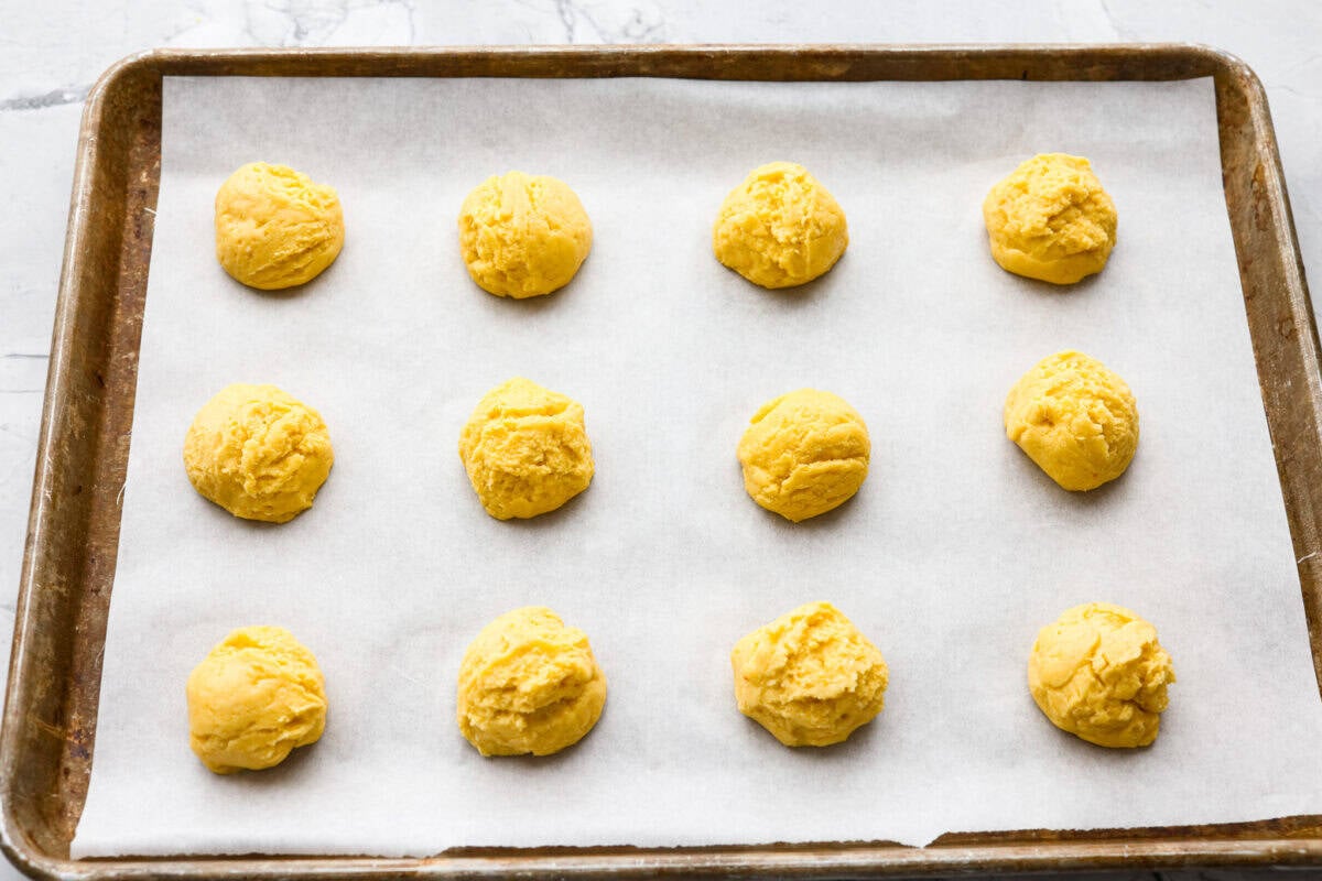 My Lemon Cake Mix Cookies are the shortcut your sweet tooth has been waiting for. Using a cake mix means you can enjoy soft, lemony cookies with a bakery-style texture in a fraction of the time. Scoops of cookie dough spread out in parchment paper on a cookie sheet.