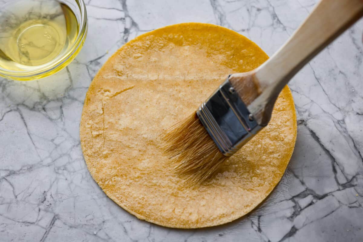 You know that moment when you’ve inhaled a basket of chips and salsa and realize… you just ate five tortillas? Yeah, same. These air fryer tortilla chips are crispy, golden, and practically guilt-free. Someone brushing olive oil onto a tortilla.