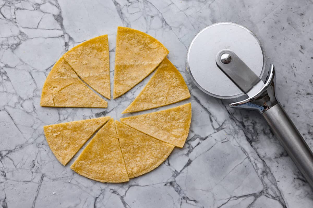 You know that moment when you’ve inhaled a basket of chips and salsa and realize… you just ate five tortillas? Yeah, same. These air fryer tortilla chips are crispy, golden, and practically guilt-free. Pizza cutter next to a tortilla cut into triangles.