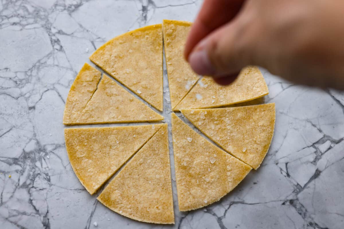 You know that moment when you’ve inhaled a basket of chips and salsa and realize… you just ate five tortillas? Yeah, same. These air fryer tortilla chips are crispy, golden, and practically guilt-free. Someone sprinkling salt onto the tortilla triangles,