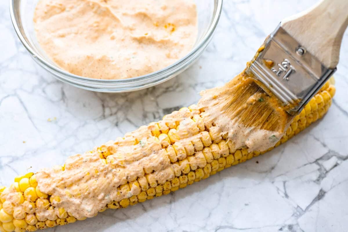 I had to try these viral Corn Ribs, and now I totally get the hype! They're fun, handheld, and smothered in creamy, zesty Mexican street corn flavor. Make a batch to share... or donโt. I wonโt judge. Someone smothering the elote sauce on the cooked corn.