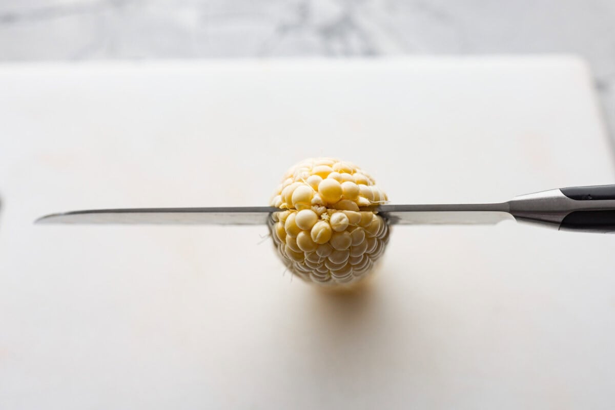 I had to try these viral Corn Ribs, and now I totally get the hype! They're fun, handheld, and smothered in creamy, zesty Mexican street corn flavor. Make a batch to share... or donโt. I wonโt judge. Overhead shot of a knife slicing through the top end of the cob.