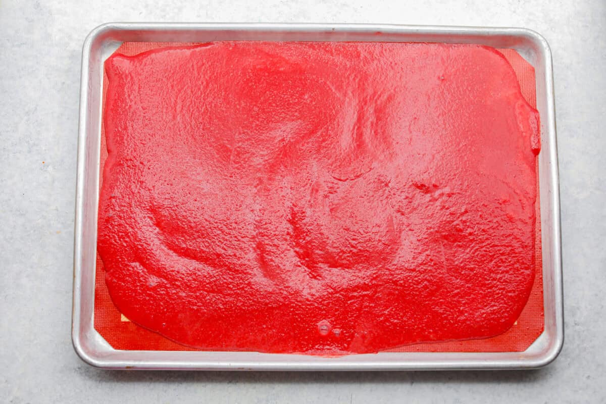 Homemade fruit leather is a fun, tasty way to turn ripe summer fruit into a snack that lasts all year! Just a few simple ingredients, no special tools, and a quick prep, then let the oven do the rest. All of the blended up ingredients smoothed out onto the silpat mat on the baking sheet.