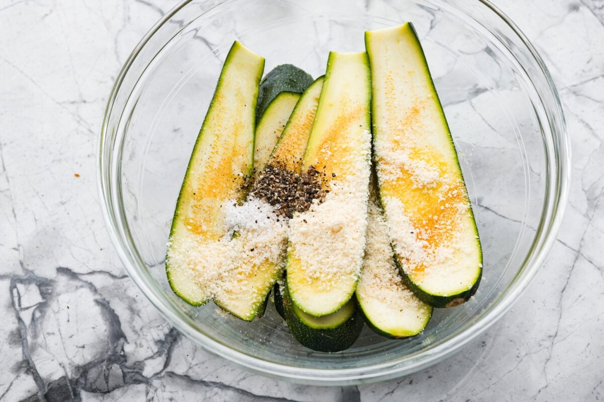 If you're not making zucchini bread with all of that home-grown zucchini, then you HAVE to try this grilled zucchini! Light, smoky, and perfectly seasoned, it cooks up in minutes and goes with just about everything. Sliced zucchini in a bowl with seasonings.