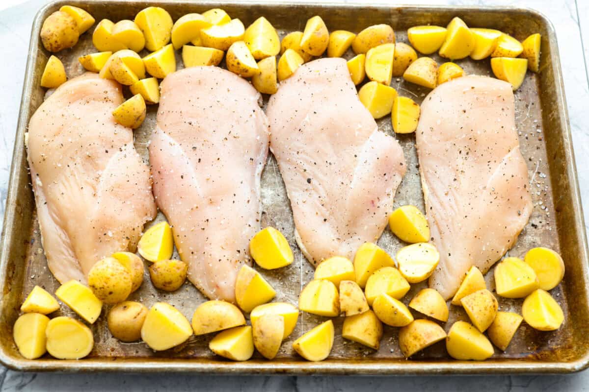 Baked buttery herb chicken with potatoes is pure comfort on a plate! I love tossing everything together in one pan and letting it cook! It saves time and lets all those delicious flavors meld for the juiciest, flavorful chicken and soft, savory potatoes. Chicken and potatoes seasoned and spread out on a baking sheet.