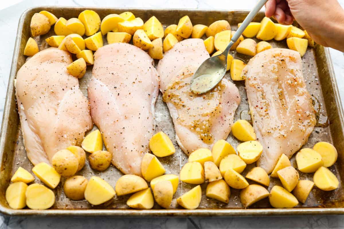 Baked buttery herb chicken with potatoes is pure comfort on a plate! I love tossing everything together in one pan and letting it cook! It saves time and lets all those delicious flavors meld for the juiciest, flavorful chicken and soft, savory potatoes. Someone spreading herb butter on the chicken and potatoes.