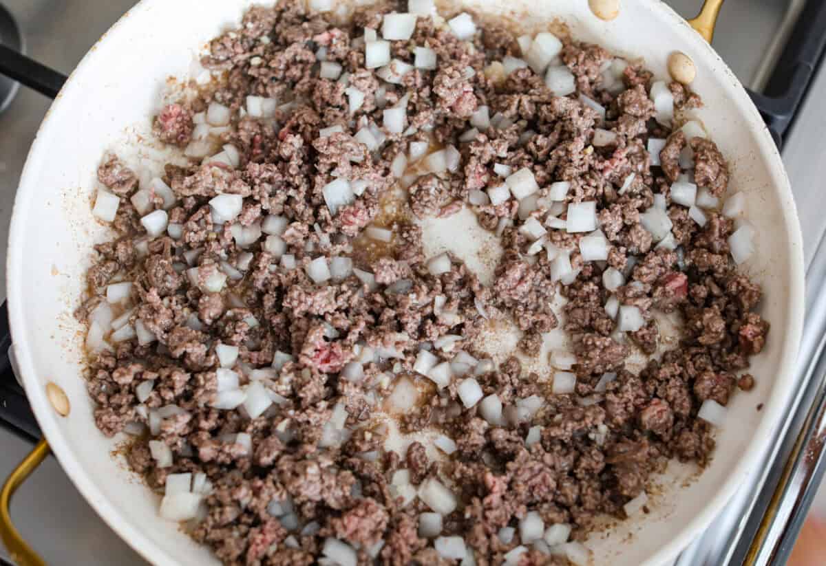 Cowboy casserole is my ultimate mom hack. Beef, cheese, corn, and tater tots, whatโs not to love? Even the picky eaters mysteriously forget how to be picky. Ground beef and onions cooking in a skillet.