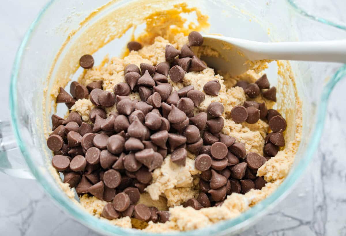 These copycat Crumbl cookies are HUGE, buttery, and loaded with melty chocolate chips. Fresh out of the oven, they just might be even better than the real deal. Bake a batch, do a taste test, and let me know if you like these better! Someone stirring in chocolate chips with a spoon.