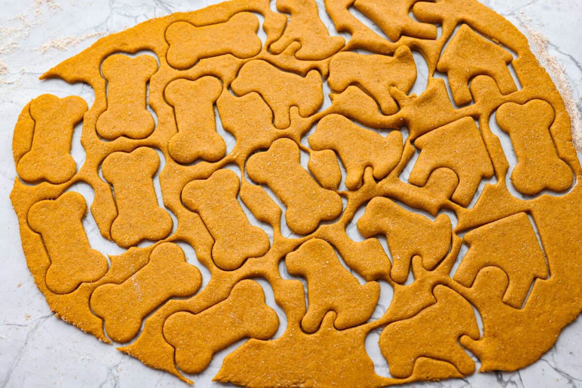 Get ready to spoil your furry friend! These homemade dog treats are made with simple ingredients and come together in no time. Your pup won’t stop begging for more! Dog treat dough rolled out and cut with cookie cutters.