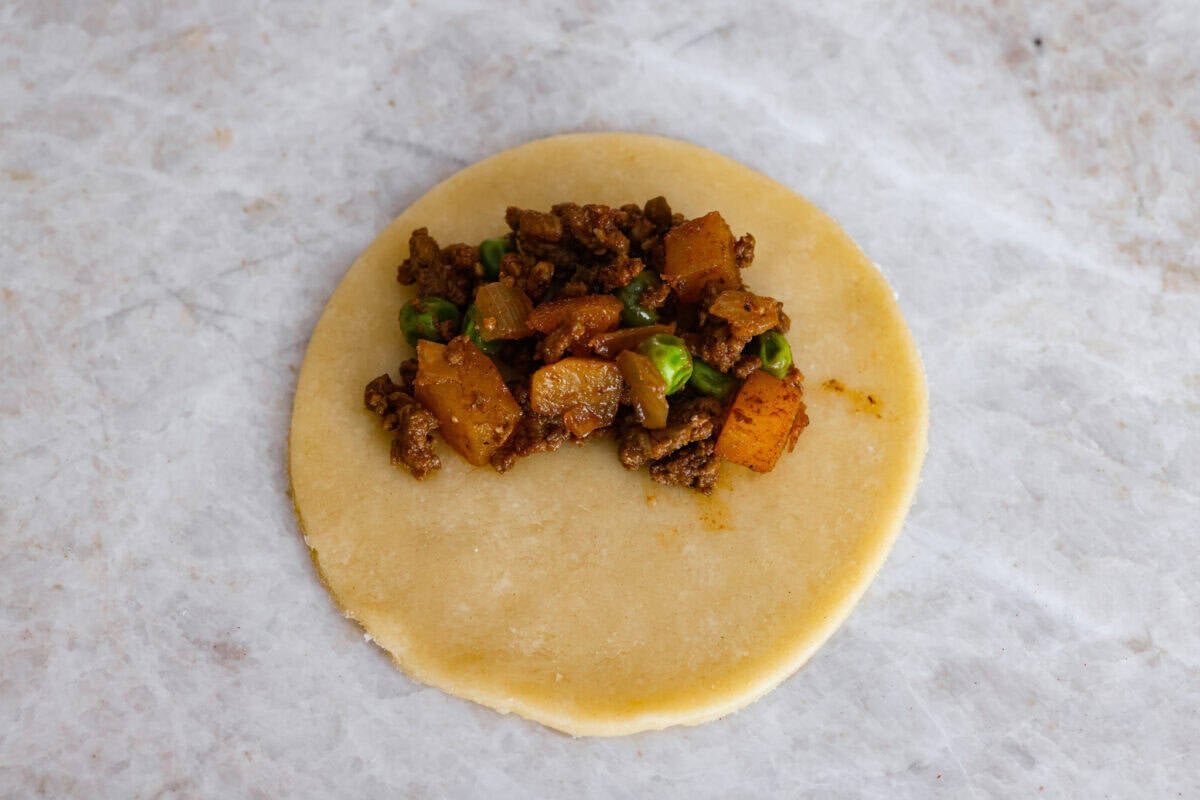 Okay, I just made homemade empanadas and Iโm obsessed! Crispy golden pockets stuffed with beef, potatoes, peas, and all the Mexican spices. You seriously need these in your life. Scoop of filling added to the circle of dough.