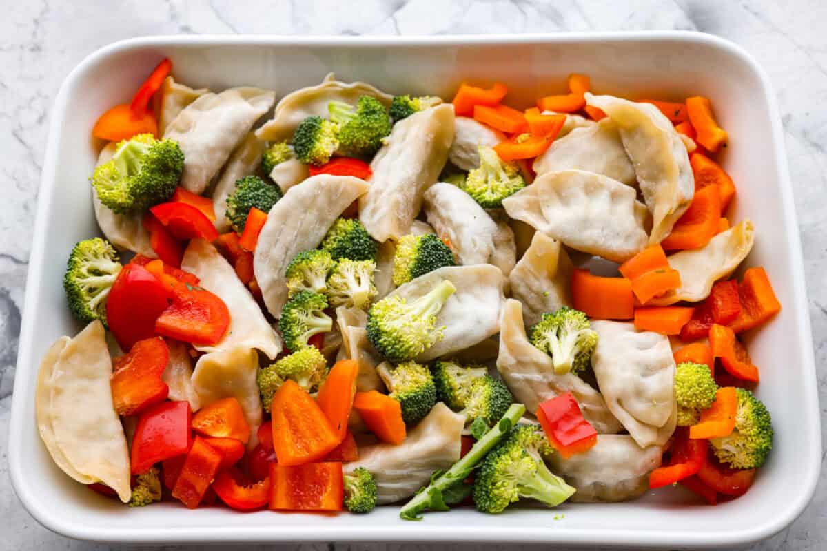 Potsticker casserole is all the tasty fun of potstickers in a warm, baked dish. Soft dumplings, fresh veggies, and a rich sauce cook together for a fast, easy, and filling meal. Potstickers added to the bottom of a casserole dish with vegetables added to the top.