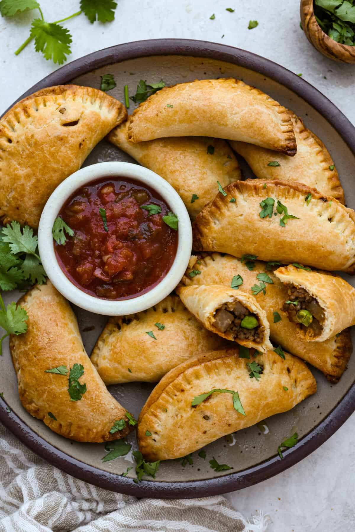 Okay, I just made homemade empanadas and Iโm obsessed! Crispy golden pockets stuffed with beef, potatoes, peas, and all the Mexican spices. You seriously need these in your life. Plate of homemade empanadas with a small bowl of salsa.