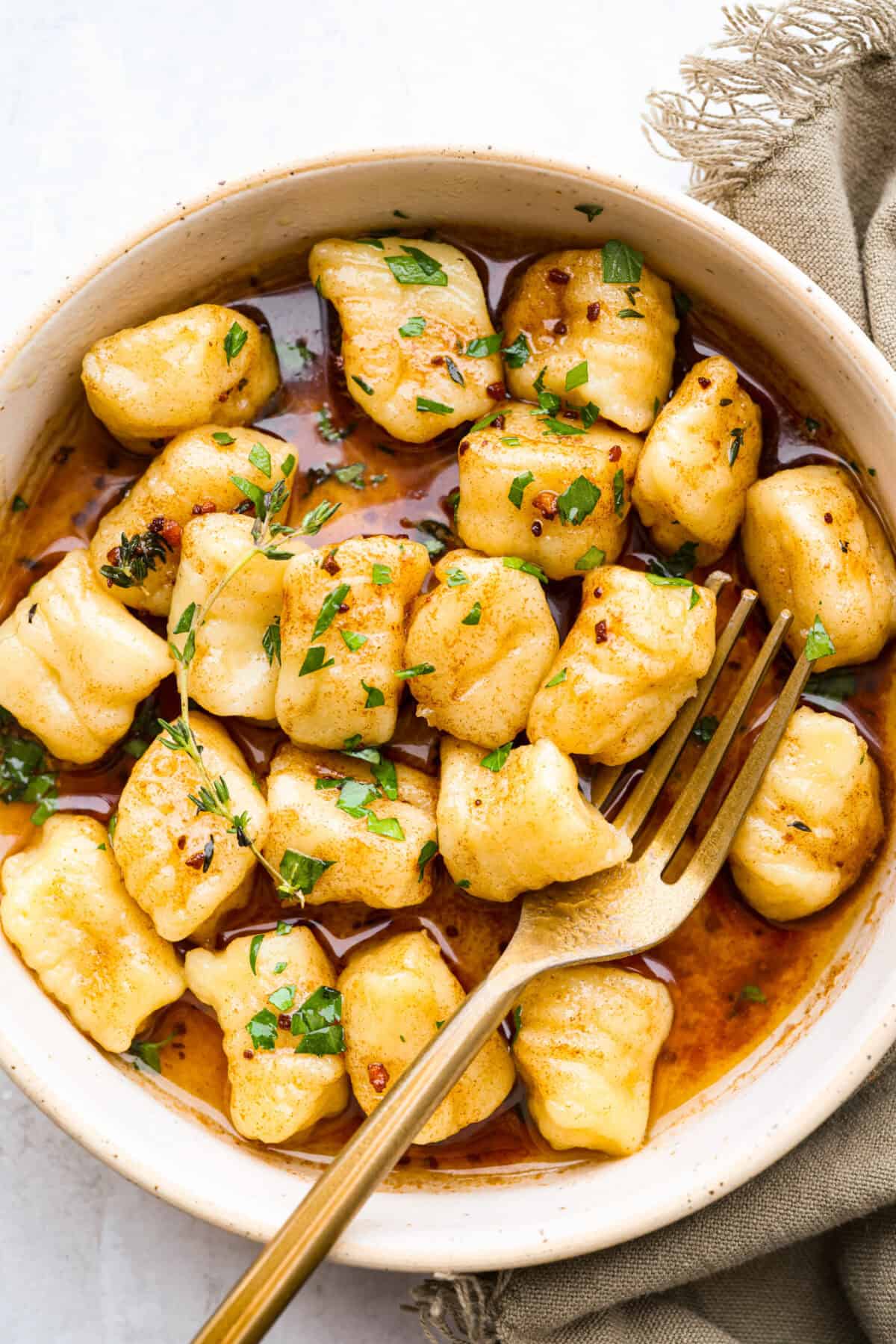 Homemade potato gnocchi is easier than you think! With just 5 simple ingredients, you can make soft, pillowy gnocchi at home. I’ll walk you through each step with clear instructions so you can master this classic Italian recipe on your first try. Bowl of cooked homemade potato gnocchi in a bowl with brown butter and herbs.