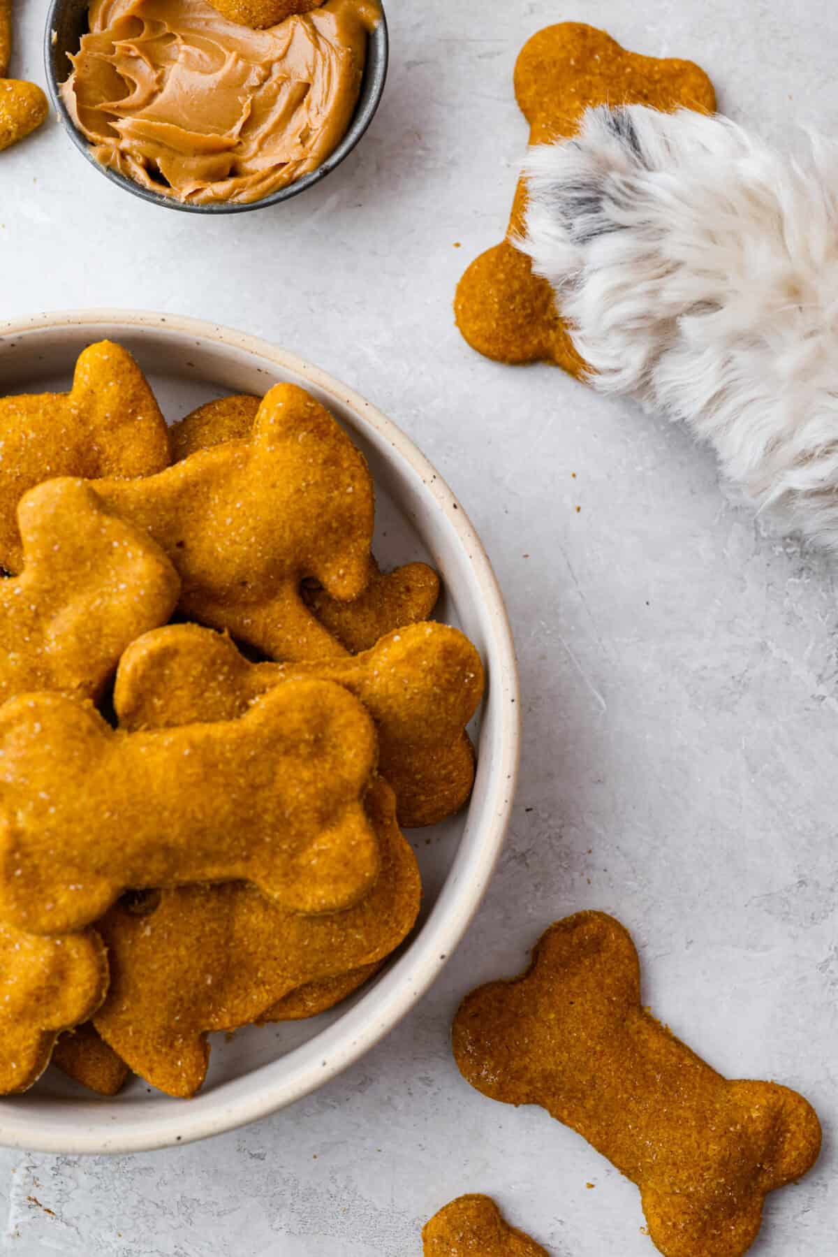Get ready to spoil your furry friend! These homemade dog treats are made with simple ingredients and come together in no time. Your pup won’t stop begging for more! Bowl of homemade dog treats next to a dog paw on a dog treat.