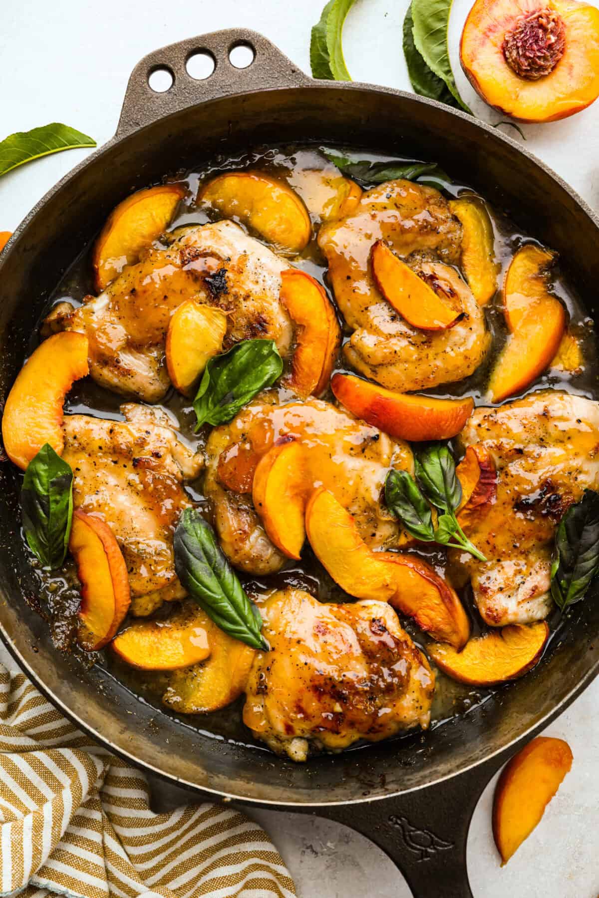 Sweet, savory, and full of summer vibes, peach chicken bakes up juicy and golden in a buttery peach preserve sauce with fresh peaches, Dijon, and a hint of garlic. Finished with basil, it’s simple, elegant, and packed with flavor! Overhead shot of peach chicken all cooked in a skillet garnished with fresh basil leaves.