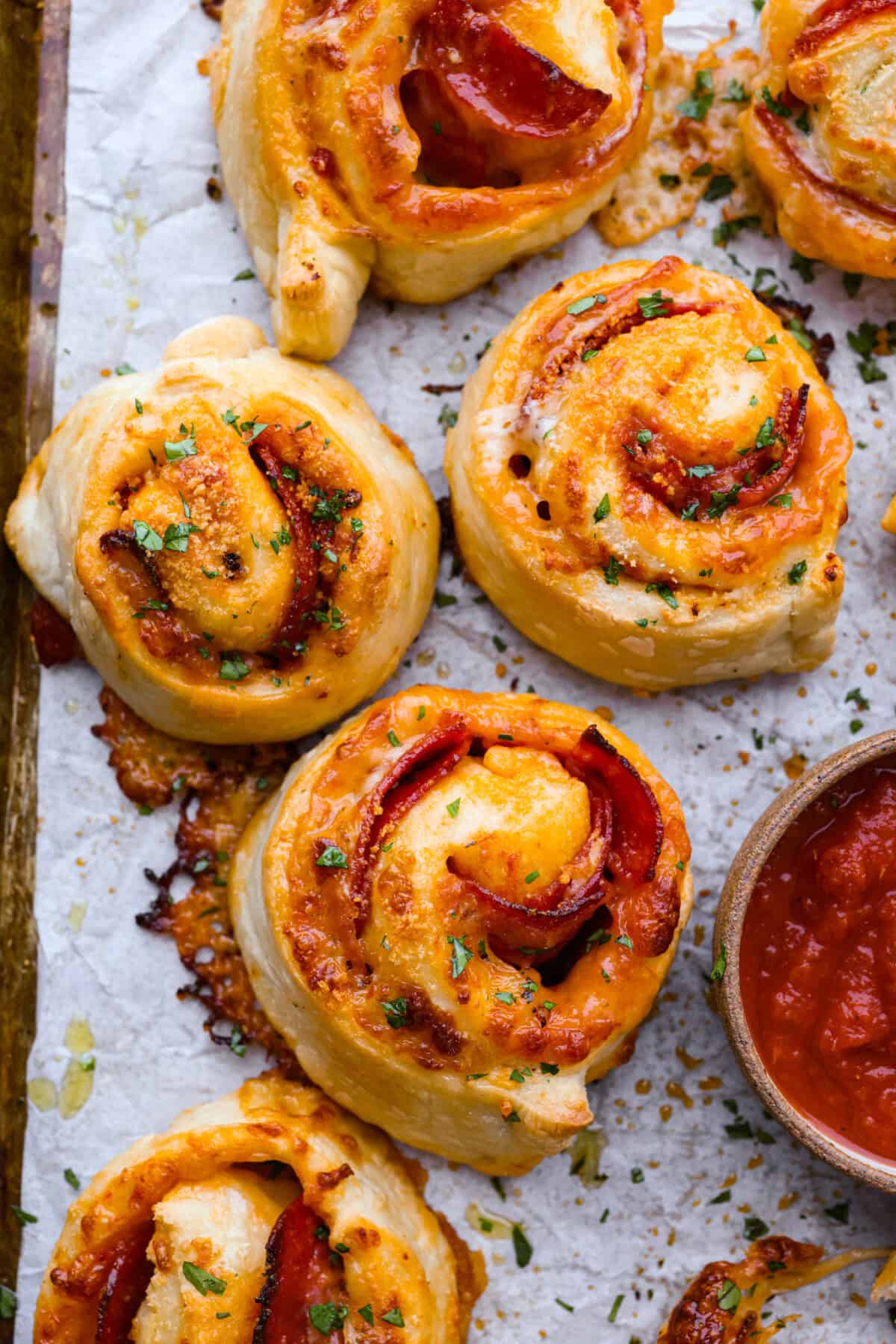 I just threw these pepperoni pizza rolls together in like 20 minutes, and my kids demolished them. AND they helped make them! You guys need to save this for a fast, fun snack or easy dinner! Overhead shot of baked pepperoni pizza rolls on the baking sheet.