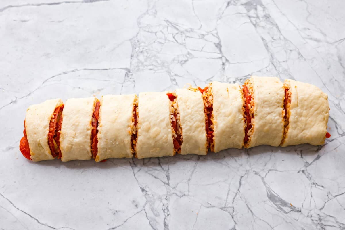 I just threw these pepperoni pizza rolls together in like 20 minutes, and my kids demolished them. AND they helped make them! You guys need to save this for a fast, fun snack or easy dinner! The buttered log cut into smaller rolls.