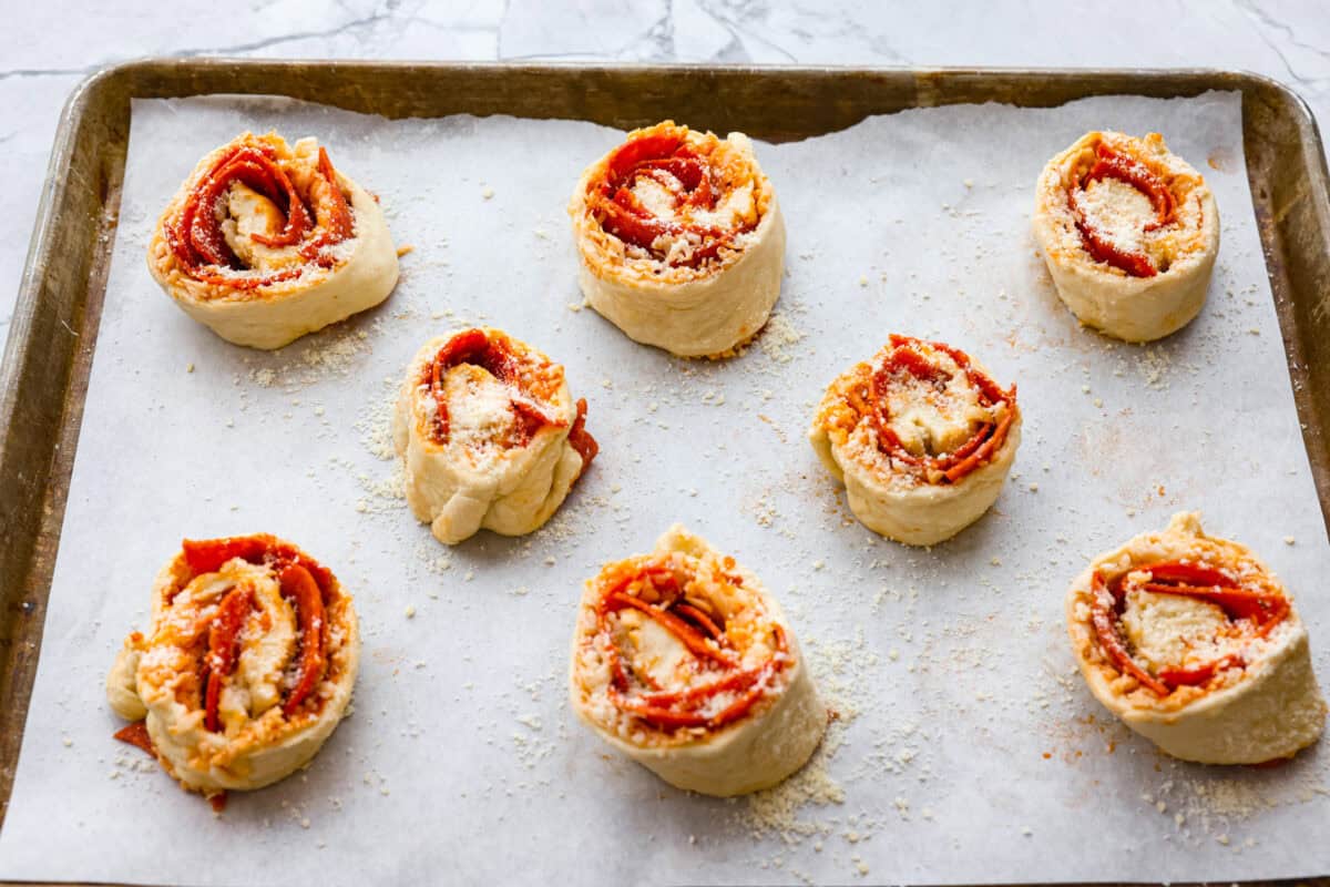 I just threw these pepperoni pizza rolls together in like 20 minutes, and my kids demolished them. AND they helped make them! You guys need to save this for a fast, fun snack or easy dinner! Pepperoni pizza rolls placed on a baking sheet with parchment paper.