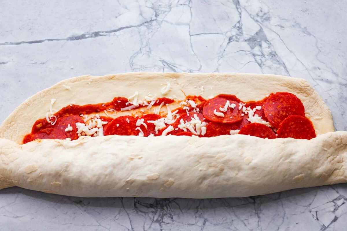 I just threw these pepperoni pizza rolls together in like 20 minutes, and my kids demolished them. AND they helped make them! You guys need to save this for a fast, fun snack or easy dinner! Rolling the dough and toppings into a log shape.