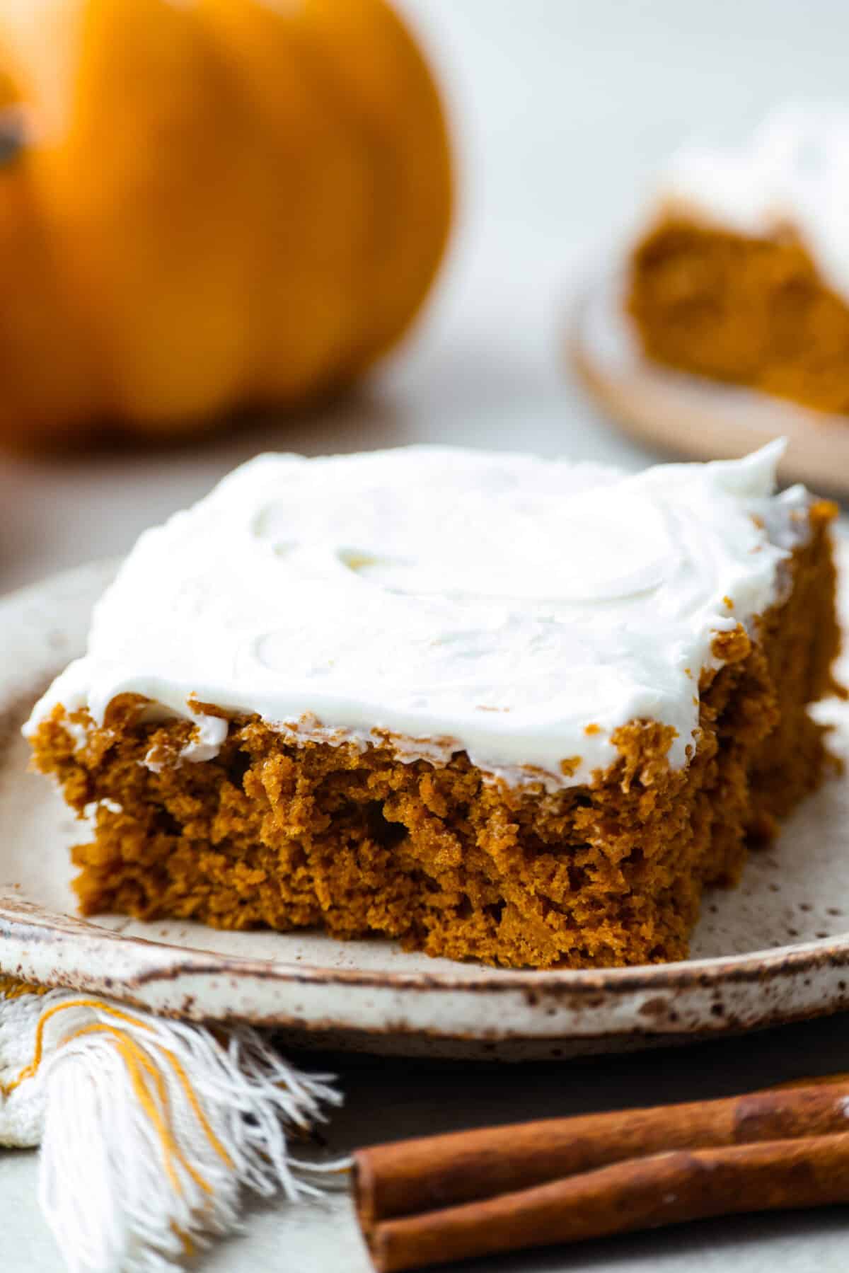 Slice of 2 ingredient pumpkin cake on a plate with cinnamon sticks in the foreground and a pumpkin in the background. 