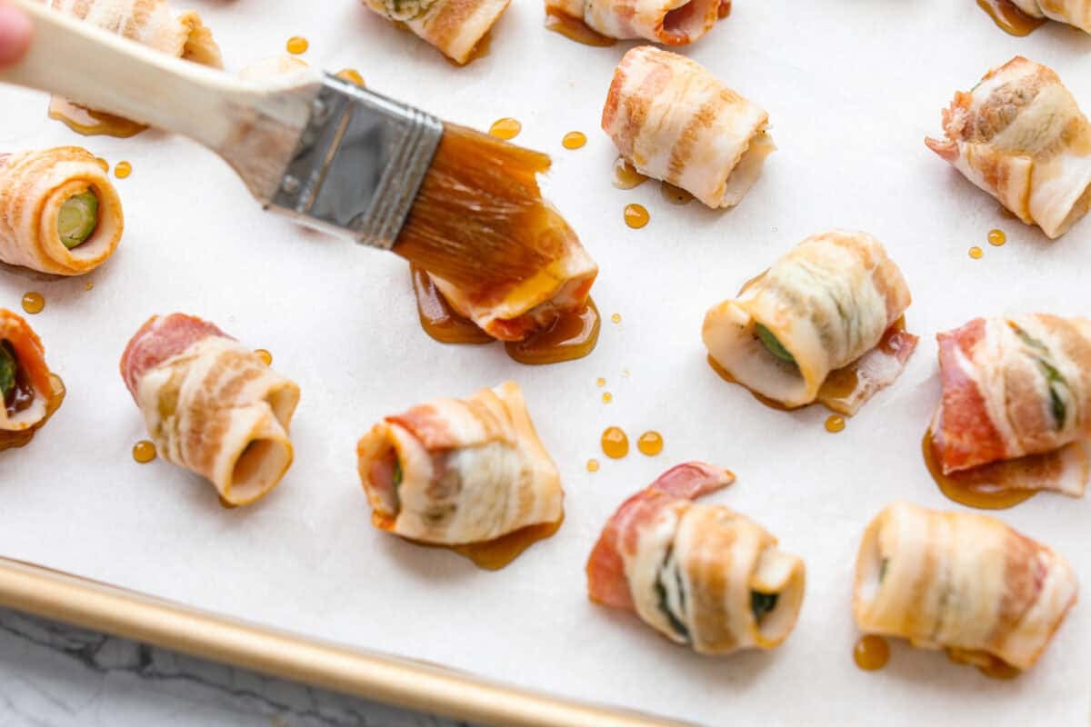 I love bacon. I love Brussels sprouts. Put them together and Iโm sold. But the secret to these bacon-wrapped Brussels sprouts? A drizzle of maple syrup! It makes them sweet, smoky, and completely irresistible. Someone brushing the maple drizzle onto the bacon wrapped Brussels sprouts.