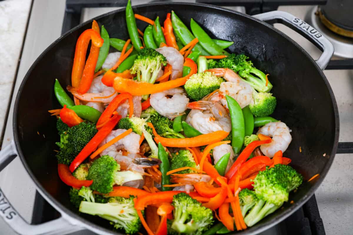 Some nights you just need dinner on the tableย fast! Thatโs when this garlic shrimp stir fry saves the day. Juicy shrimp, crisp veggies, and the BEST garlicky sauce all come together in 20 minutes. Shrimp added to the veggies in the wok.