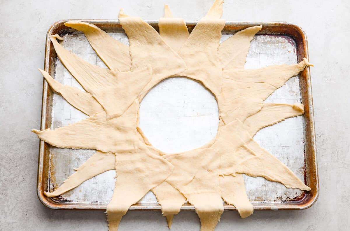 Pizza night just got a glow-up!ย This fun pull-apart pizza ring is perfect for family dinner, game day, or a party snack. Easy to make, endlessly customizable, and totally kid-approved, youโll be reaching for slice after slice! Triangles of crescent dough arranged in a sunburst shape on a cookie sheet.