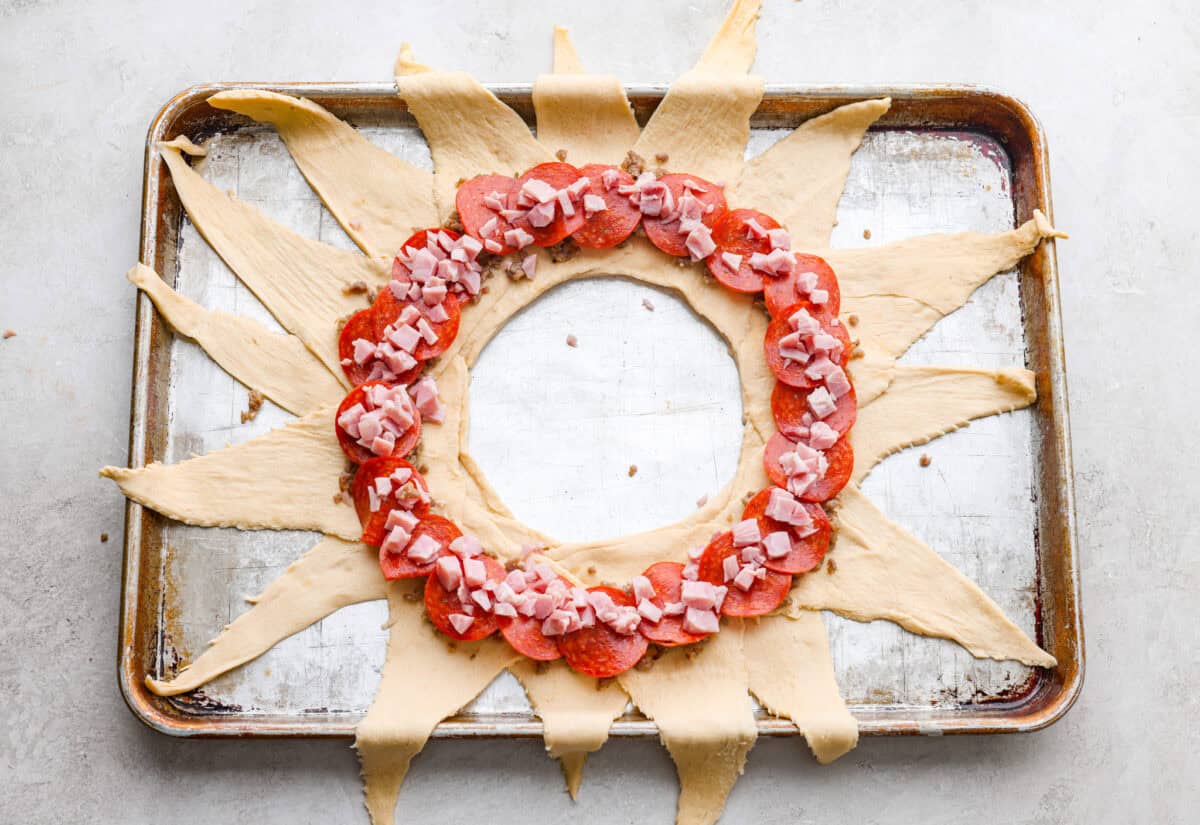 Pizza night just got a glow-up!ย This fun pull-apart pizza ring is perfect for family dinner, game day, or a party snack. Easy to make, endlessly customizable, and totally kid-approved, youโll be reaching for slice after slice! sauce and toppings in a ring on the sunburst crescent dough shape.